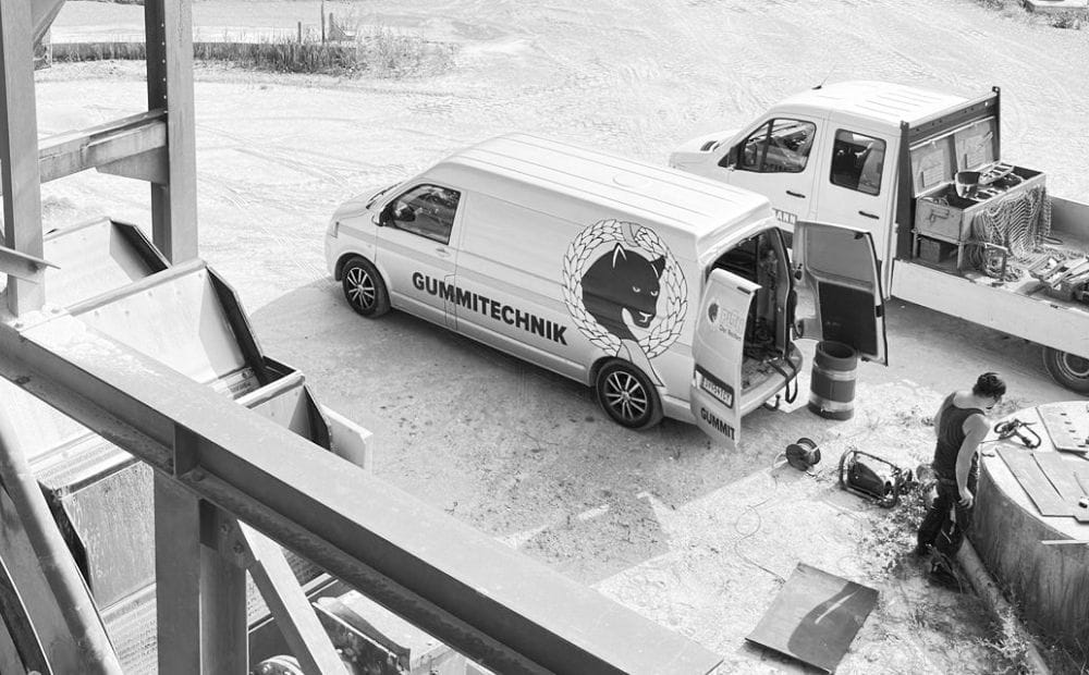 Zwei Servicefahrzeuge, eines mit der Aufschrift ‚Gummitechnik‘, parken bei einem Arbeitseinsatz im Außenbereich einer Industrieanlage.