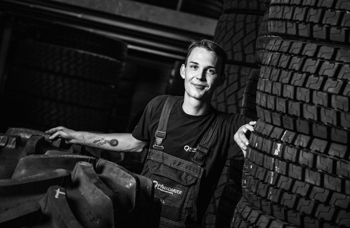 Mitarbeiter von Plankenauer steht zwischen aufgestapelten Reifen – persönlicher Service und Expertise im Reifenlager.