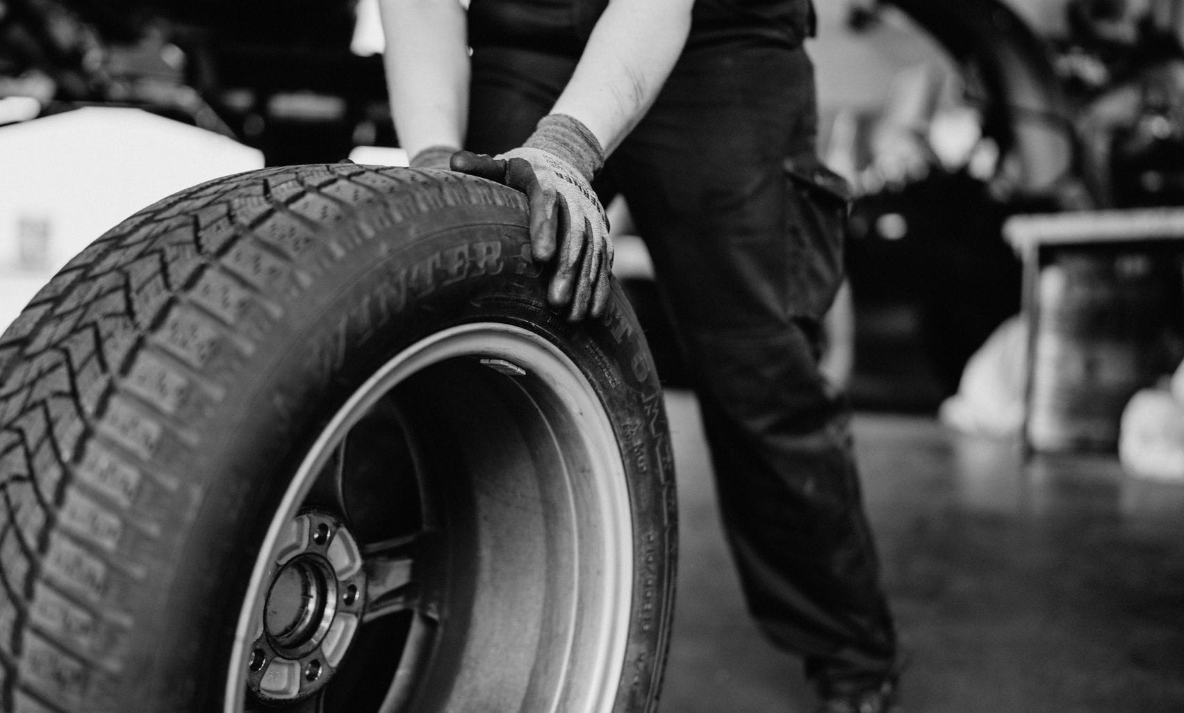 Ein Mitarbeiter rollt einen Reifen durch die Werkstatt, eine Hand greift nach dem Reifen.