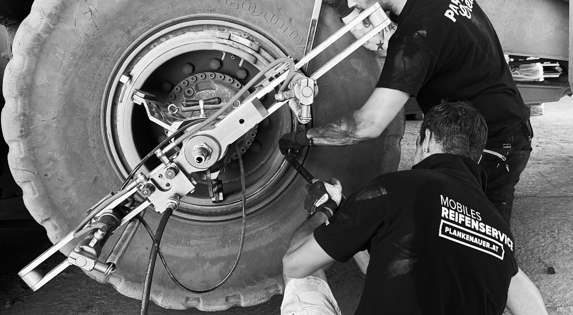 Zwei Plankenauer-Mitarbeiter arbeiten mit einem Gerät am Reifen eines Fahrzeugs – mobiler Reifenservice direkt vor Ort.