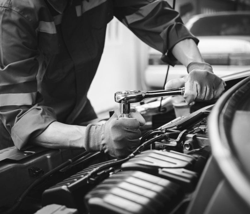 Ein Mechaniker arbeitet konzentriert an einem geöffneten Motorraum in der Werkstatt.