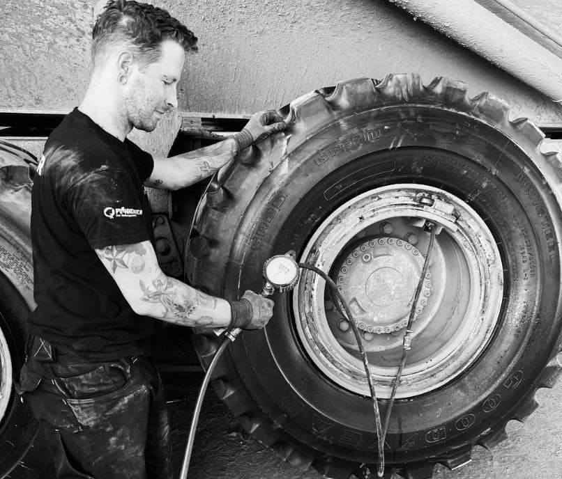 Ein Mitarbeiter wuchtet ein Autoreifenrad mit einer professionellen Auswuchtmaschine.