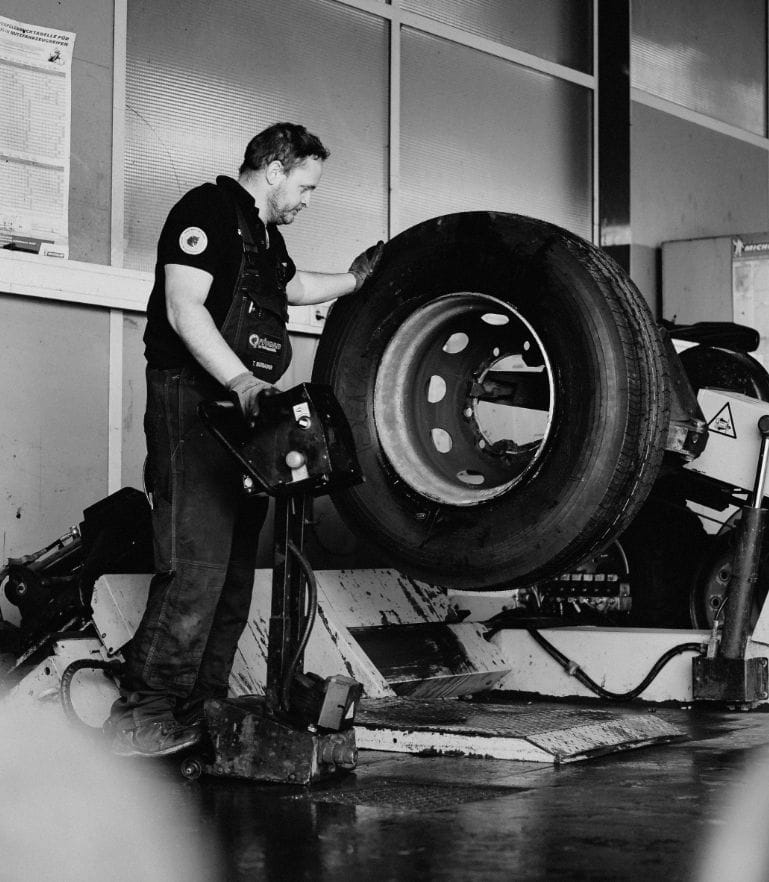 Ein Monteur arbeitet an einer großen Montagemaschine und setzt einen Lkw-Reifen auf eine Felge.