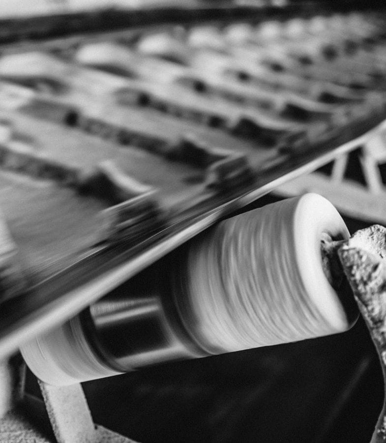 Detailaufnahme einer sich drehenden Rolle unter einem laufenden Förderband mit Gummilamellen.