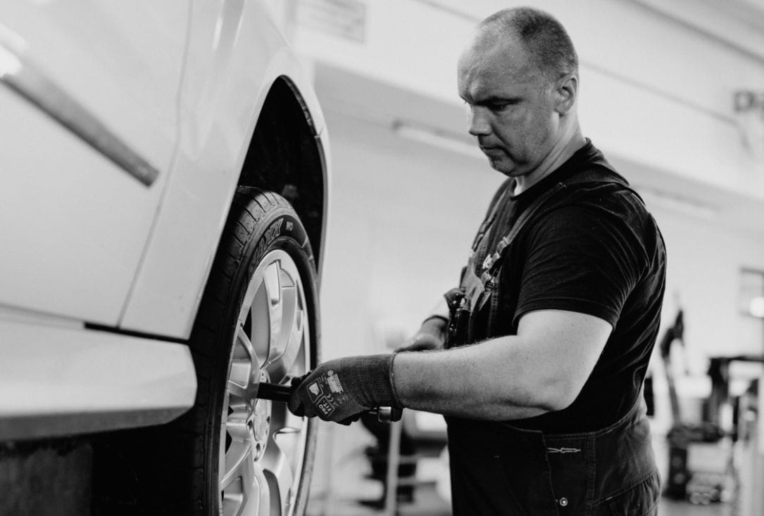 Ein Monteur zieht mit einem Werkzeug die Radschrauben an einem aufgebockten Fahrzeug fest.