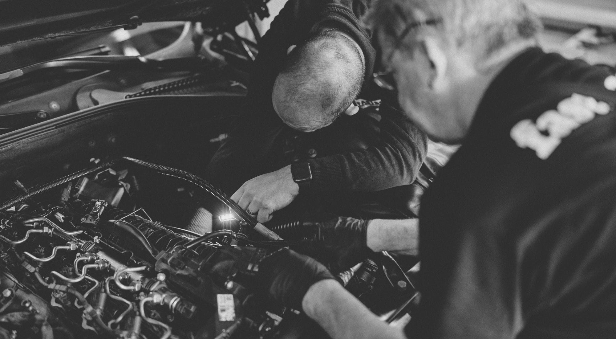 Zwei Mechaniker arbeiten gemeinsam am Motorraum eines Fahrzeugs in der Fastbox.