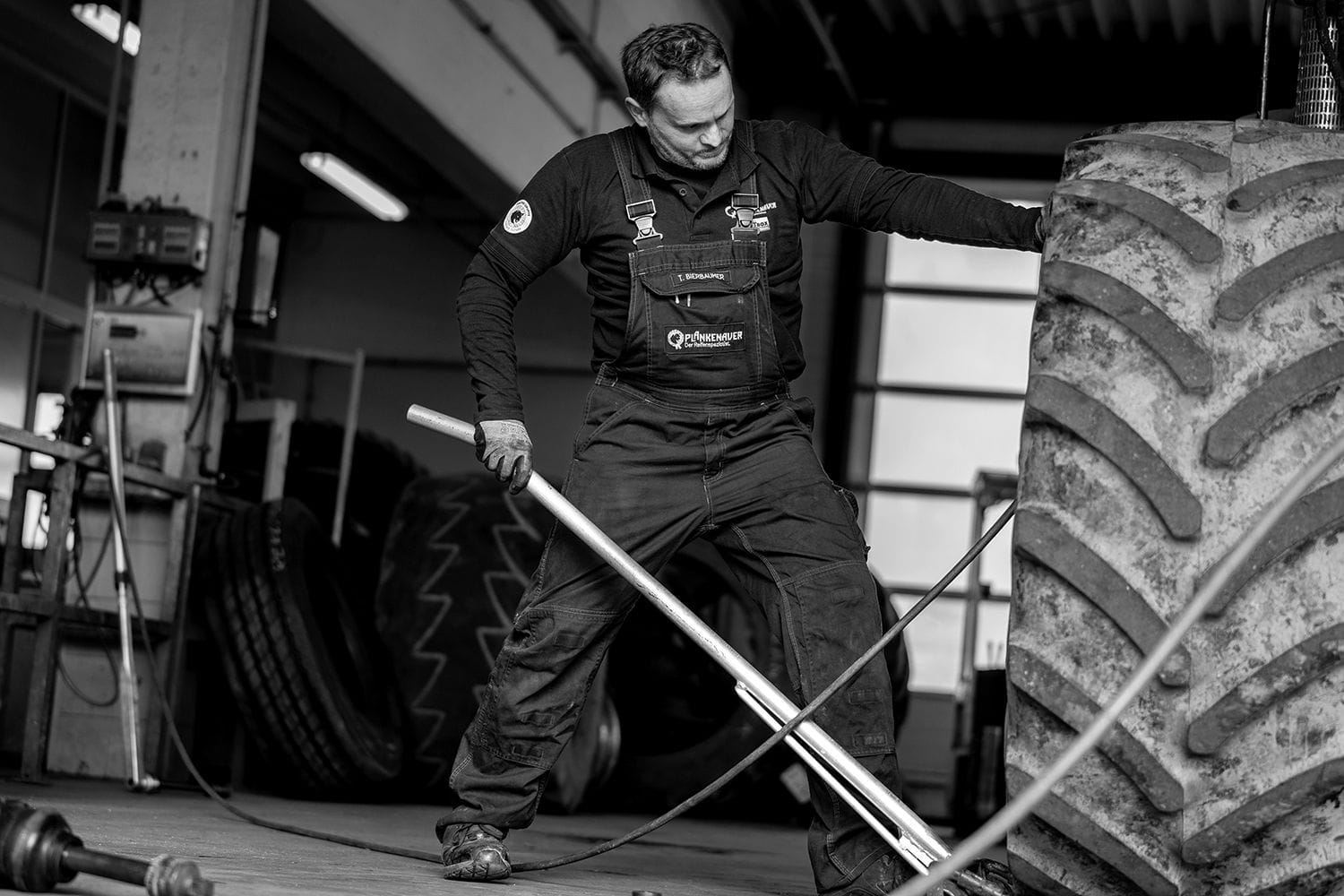 Ein Reifenmonteur in Arbeitskleidung verwendet eine lange Metallstange, um einen großen Traktorreifen zu bearbeiten.