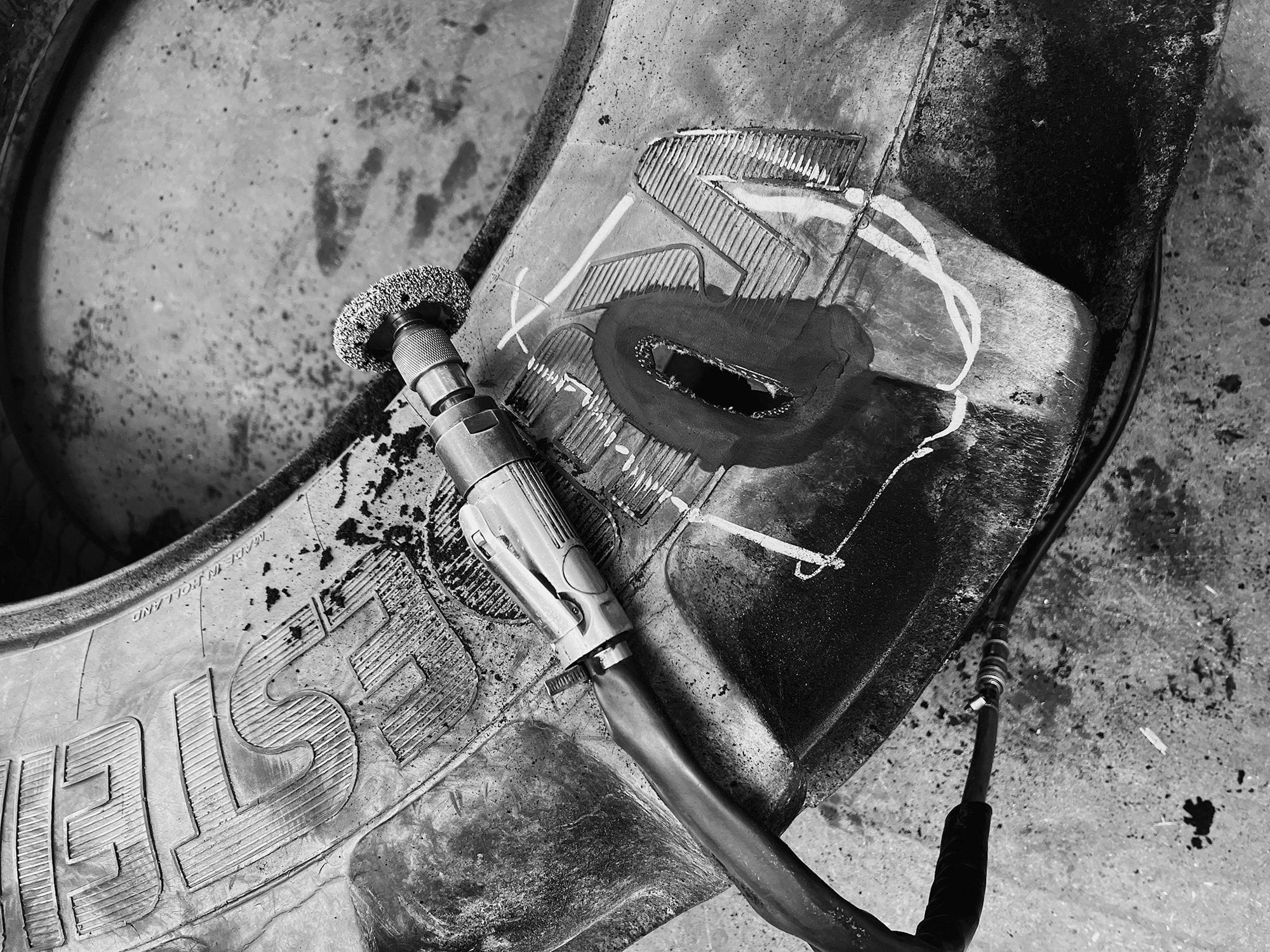 Nahaufnahme einer beschädigten Stelle an einem großen Reifen, die mit Spezialwerkzeug für eine Reparatur vorbereitet wird.