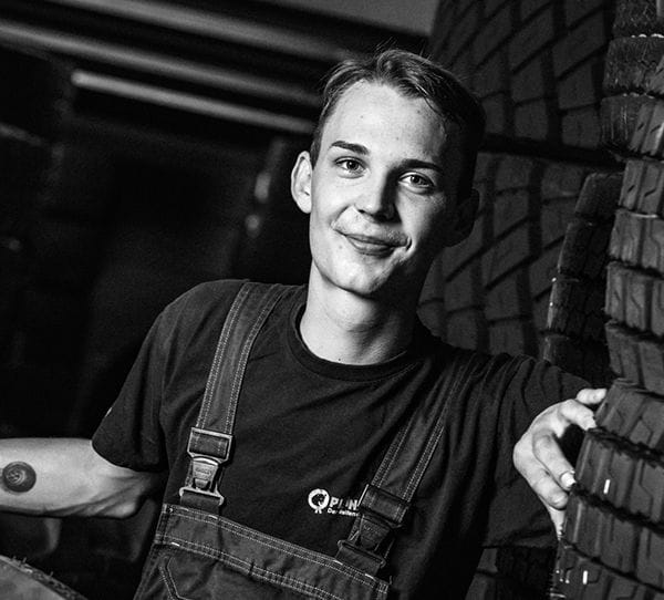 Lächelnder Mitarbeiter in schwarzem Shirt steht in einer Werkstatt und symbolisiert Karrieremöglichkeiten.